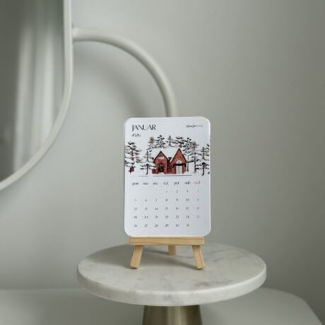 Elegant January 2026 desk calendar with winter village design on a small wooden stand.