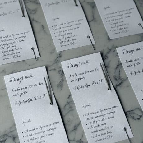 Elegant wedding program cards with handwritten-style calligraphy, set on a marble surface.