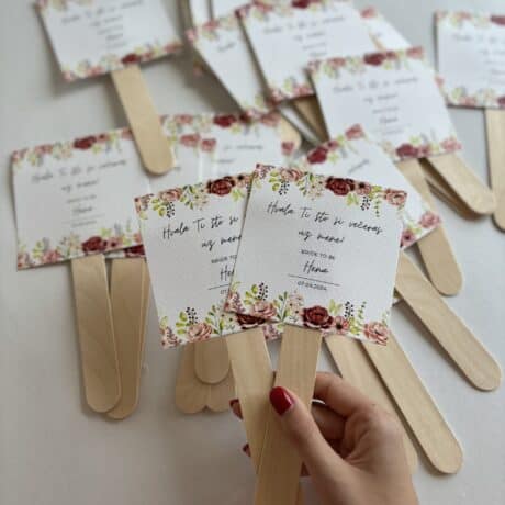 Colorful wedding program fans with floral design and wooden handles for wedding celebration.