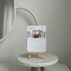 Elegant January 2026 desk calendar with winter village design on a small wooden stand.