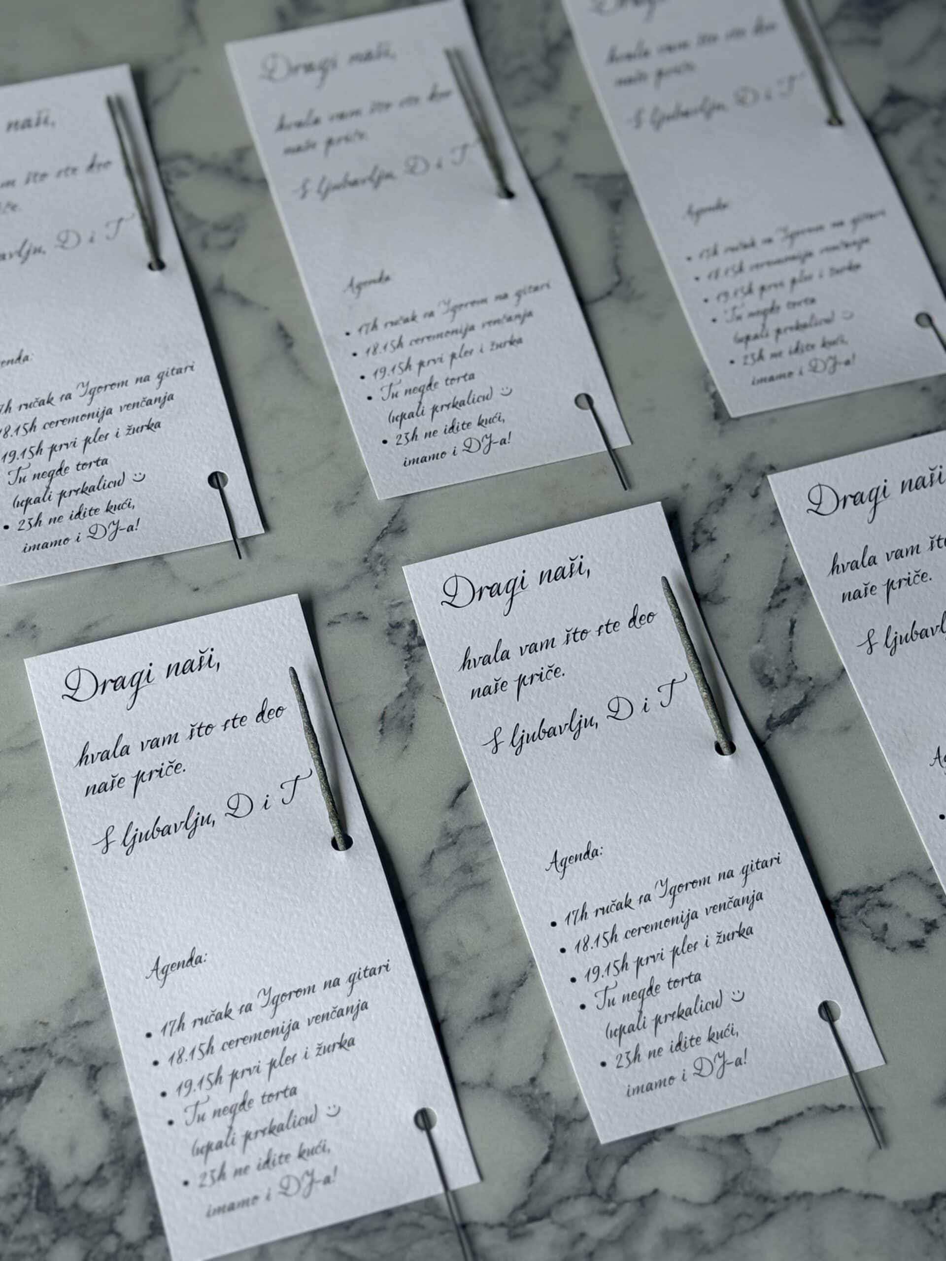 Elegant wedding program cards with handwritten-style calligraphy, set on a marble surface.