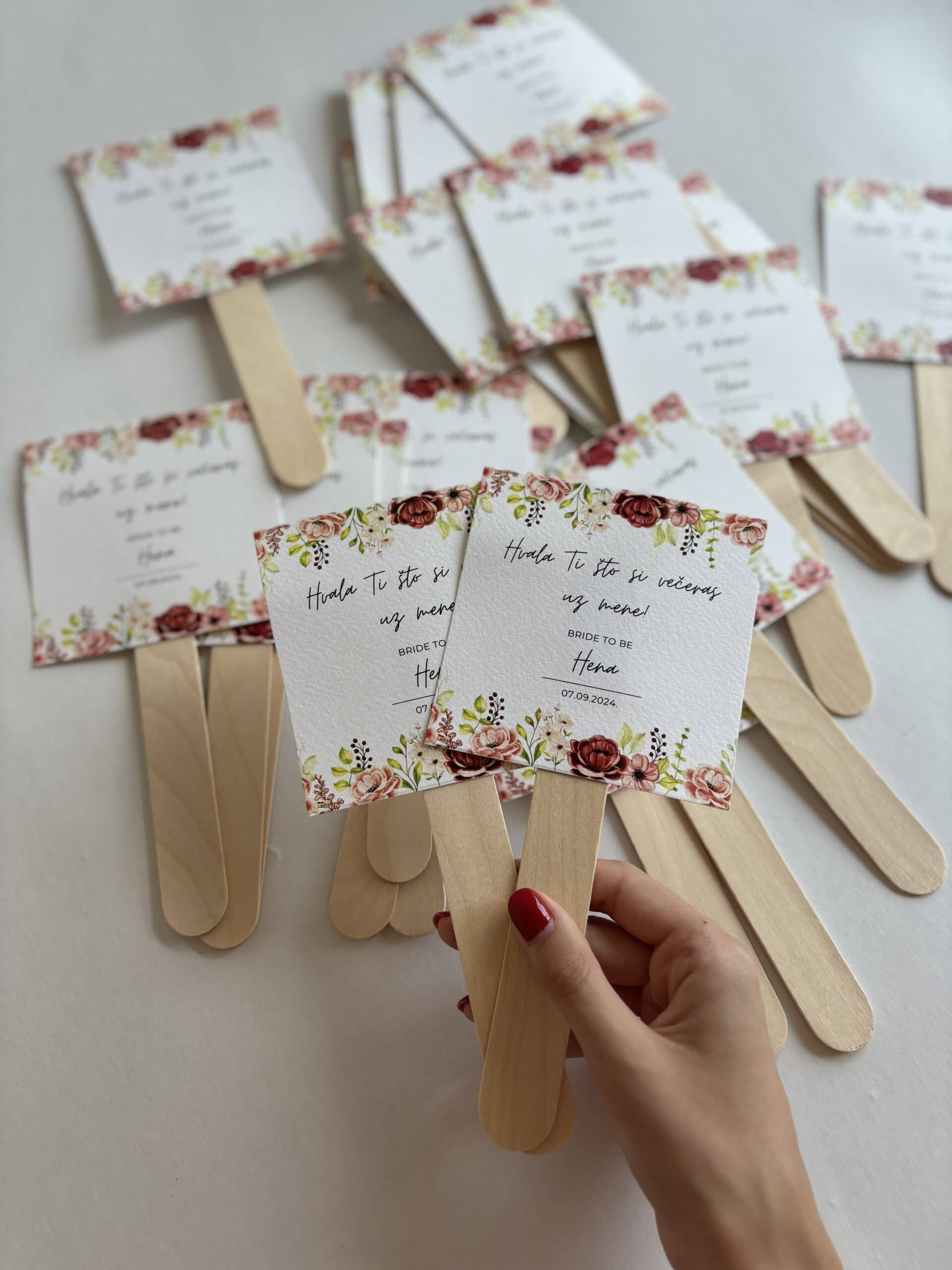 Colorful wedding program fans with floral design and wooden handles for wedding celebration.